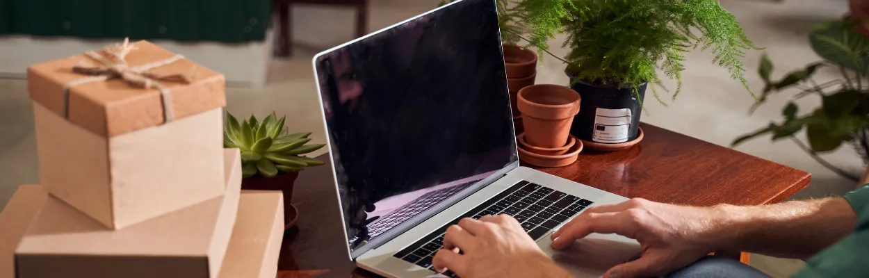 Mężczyzna siedzący przy biurku na którym znajdują się książki, laptop i pudełko prezentowe