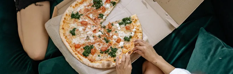 Pizza w kartonie leżącym na kanapie pomiędzy dwiema kobietami